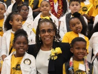 Woman of color stands with several elementary age children of color at a CDU event