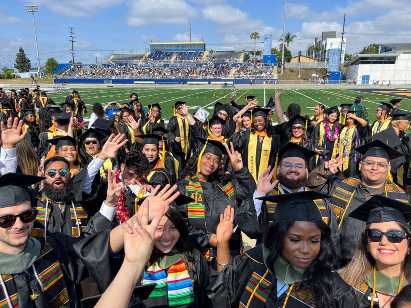 Group photo of CDU graduates waving at the camera as they line up to grab their seats at Commencement.