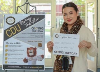 CDU staff members holds sign saying "I give back because other contributed to my education too" during CDU Giving Tuesday.