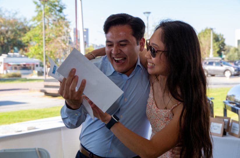 student holding match letter while being hugged by family