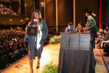 student-wearing-regalia-and-holding-degree